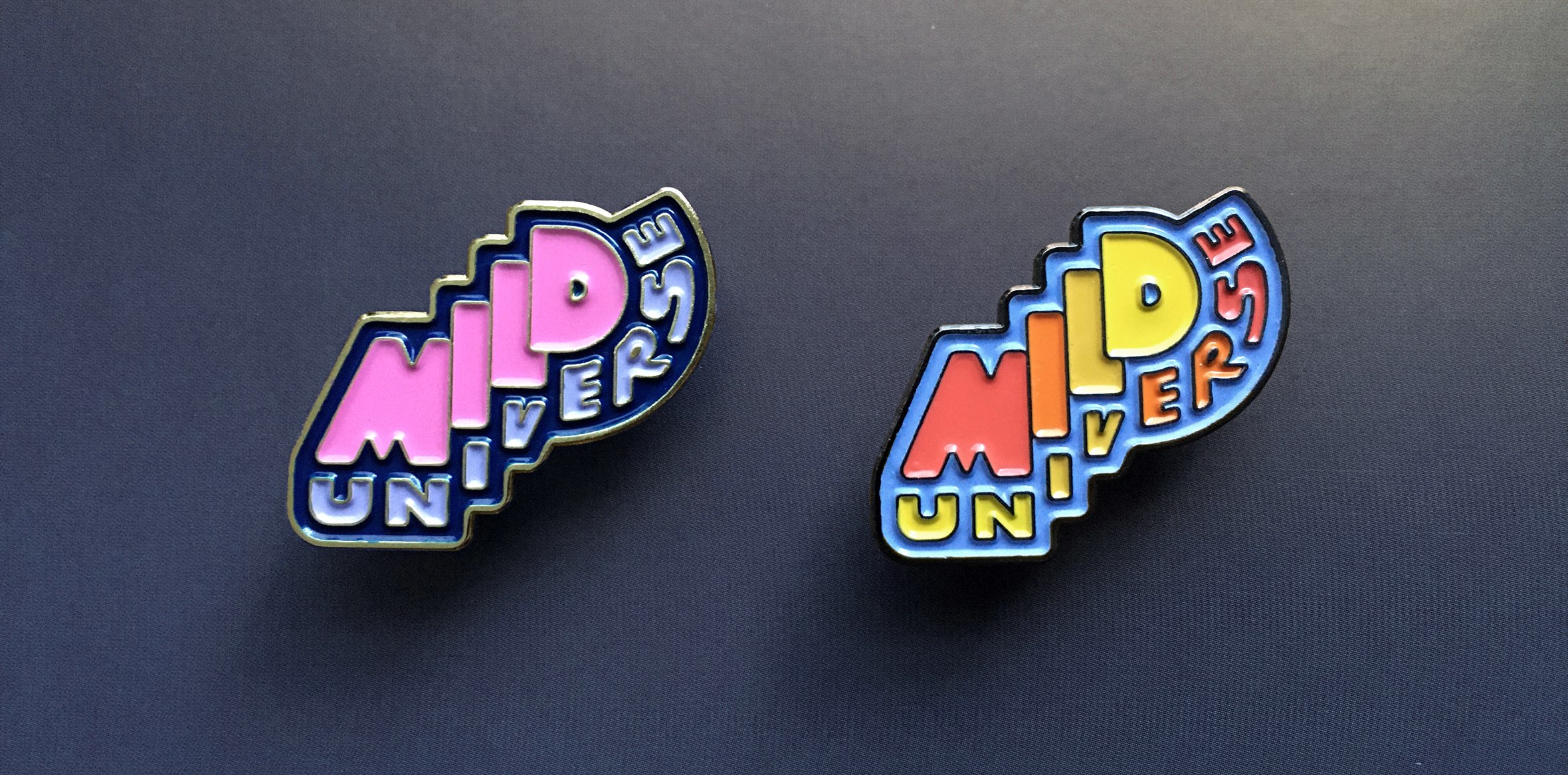 Enamel pins featuring the Mild Universe logo design in both 'Space Candy' and '70's Dinnerware' colorways